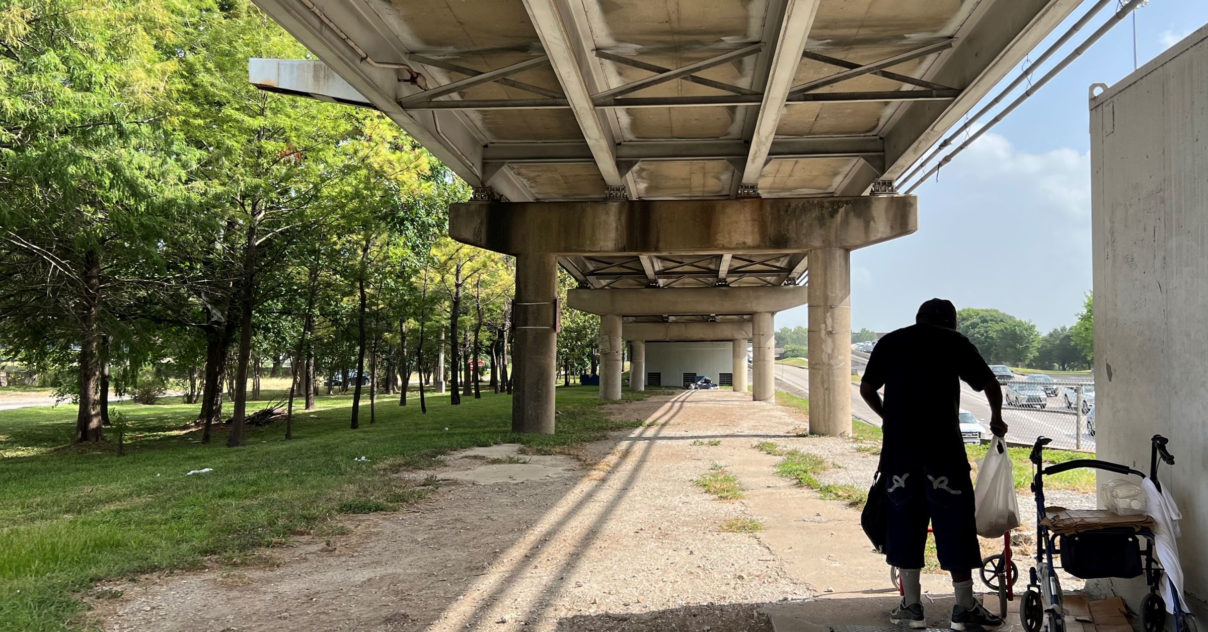 A homeless person under a bridge adds items to their cart.